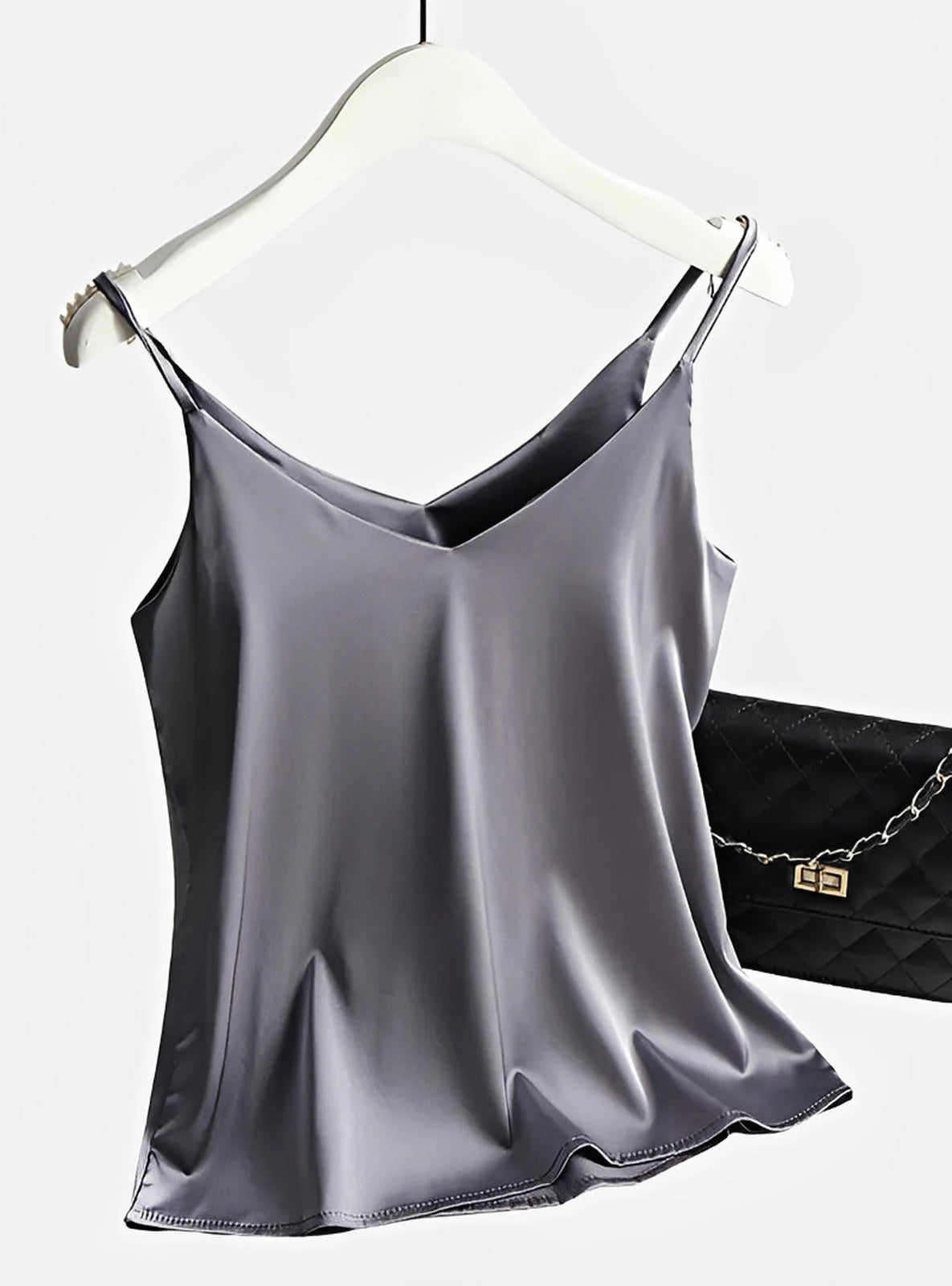 Silver satin camisole top with thin straps, displayed on hanger next to quilted purse