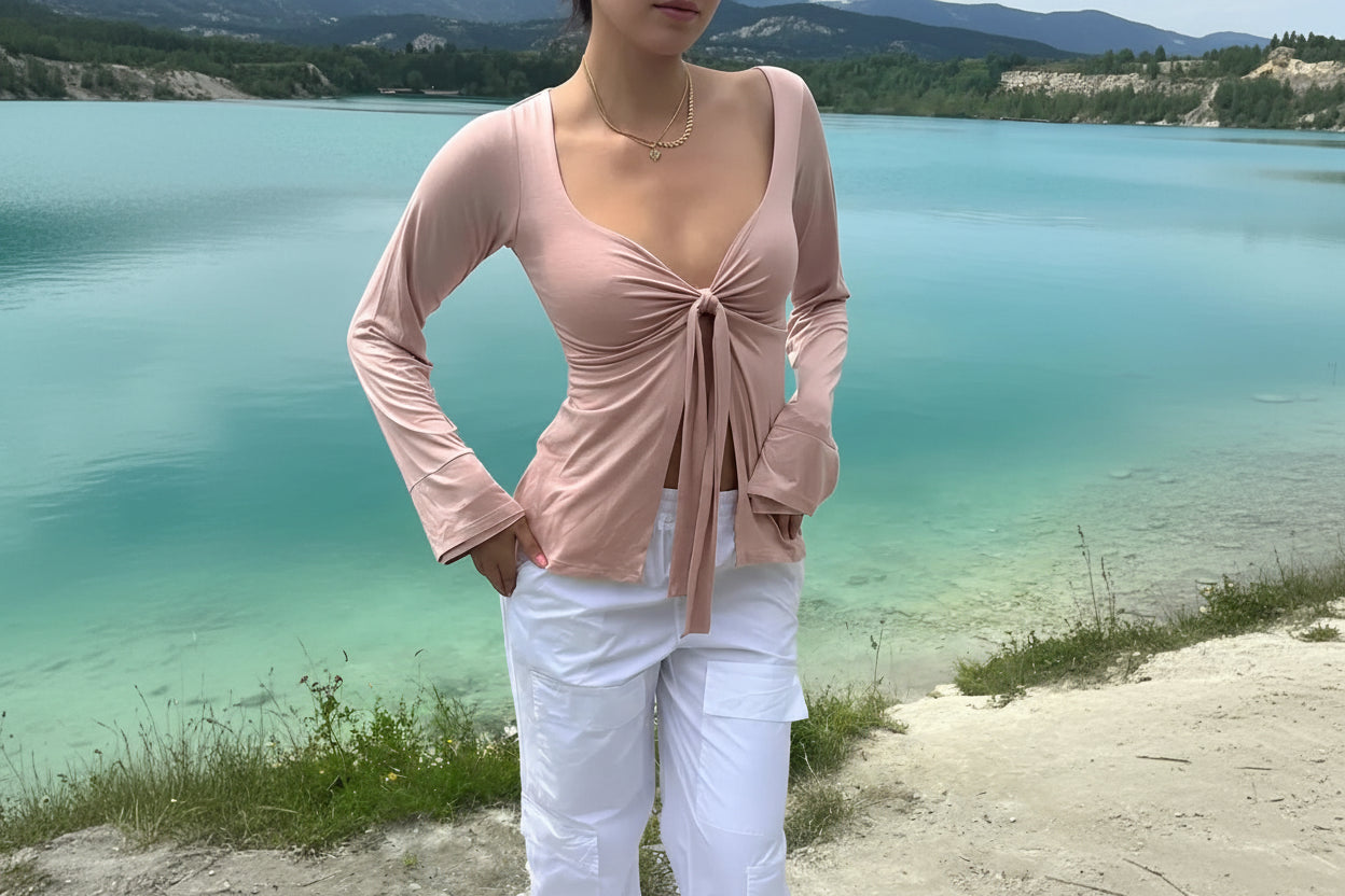Woman in a pink tie-front long sleeve top and white cargo pants by a lake