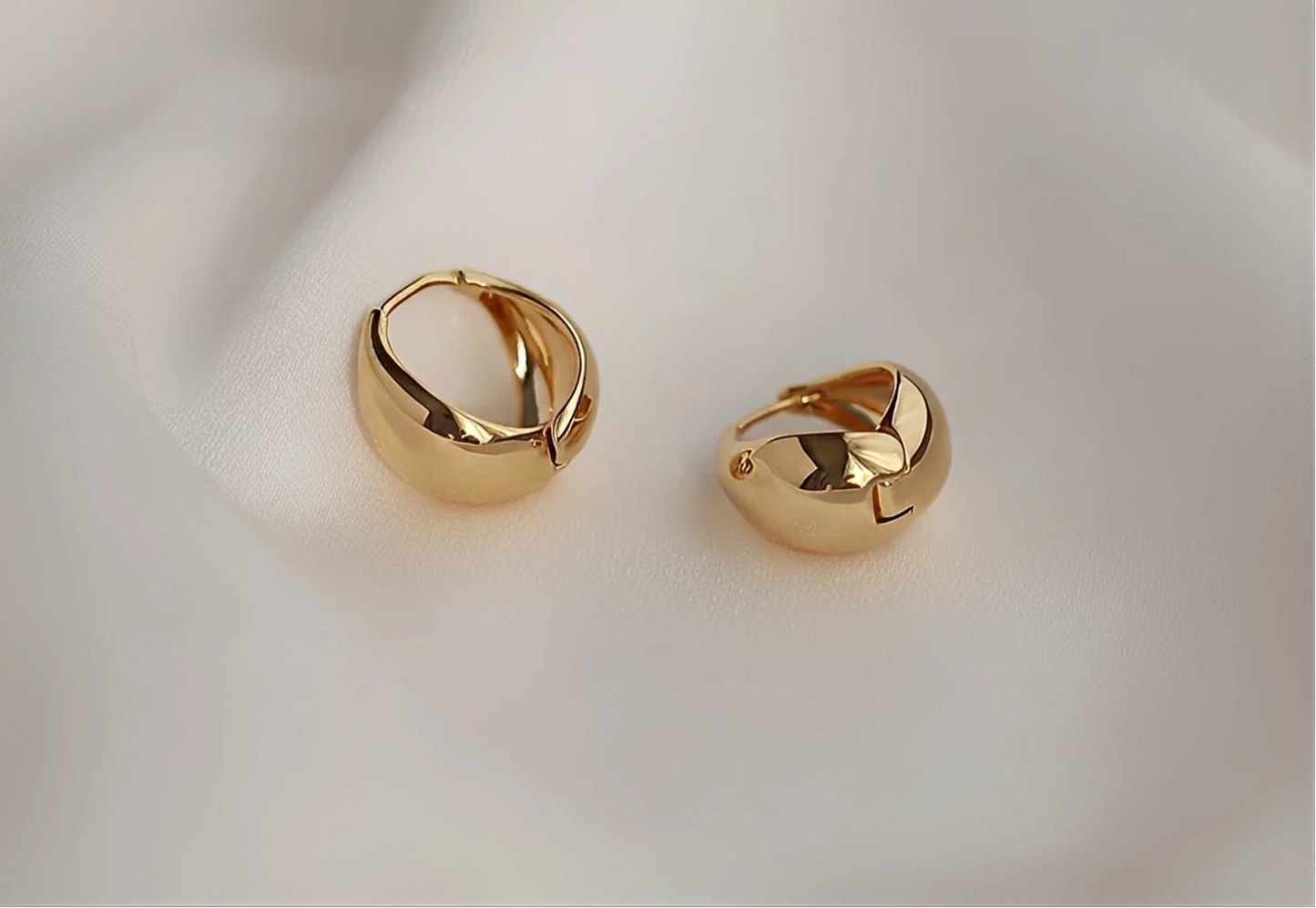Pair of chunky gold hoop earrings on soft white fabric background