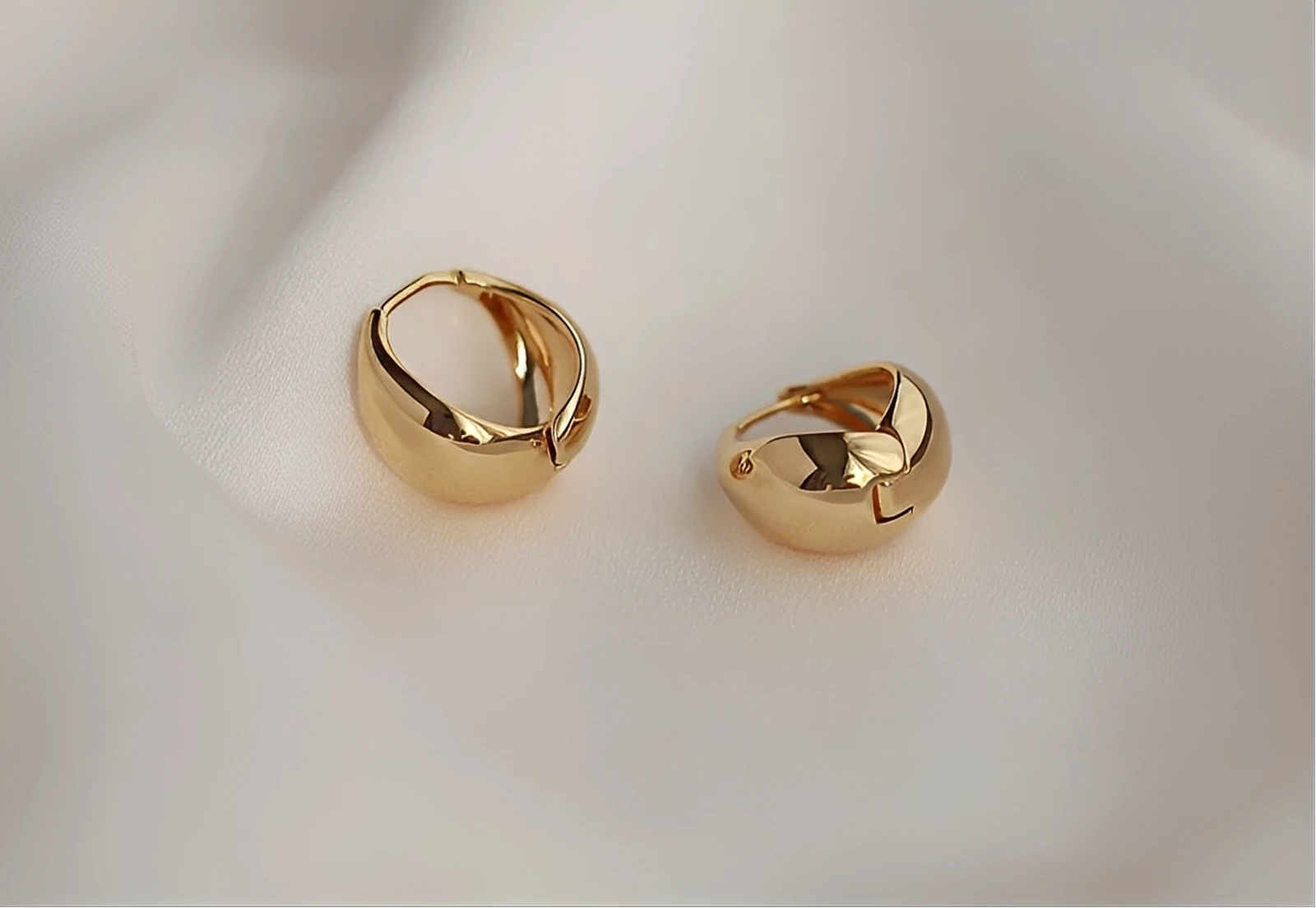 Pair of chunky gold hoop earrings on soft white fabric background
