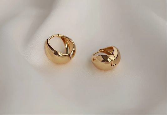 Pair of chunky gold hoop earrings on soft white fabric background