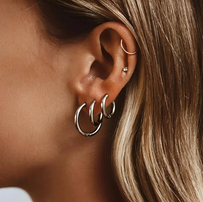 Three silver hoop earrings and gold ear cuff on ear with blonde hair