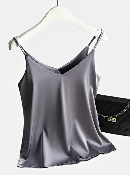 Silver satin camisole top with thin straps, displayed on hanger next to quilted purse