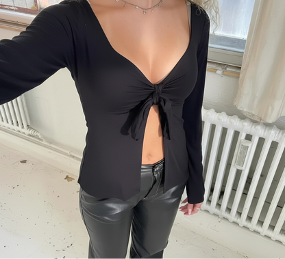 Woman wearing a black tie-front long sleeve crop top and black faux leather pants