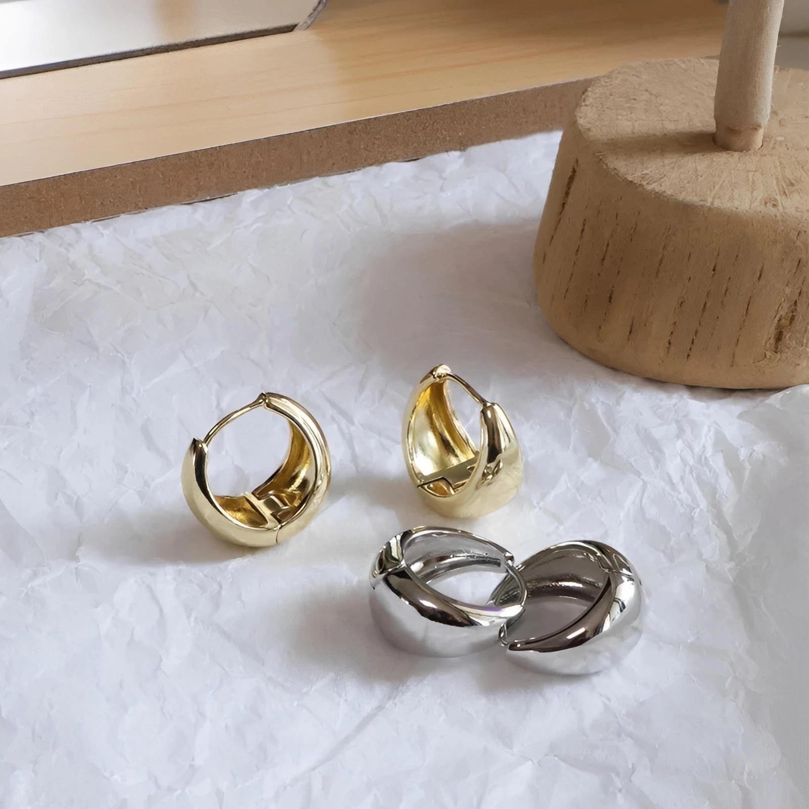 Chunky gold and silver hoop earrings on textured white surface, modern jewelry style