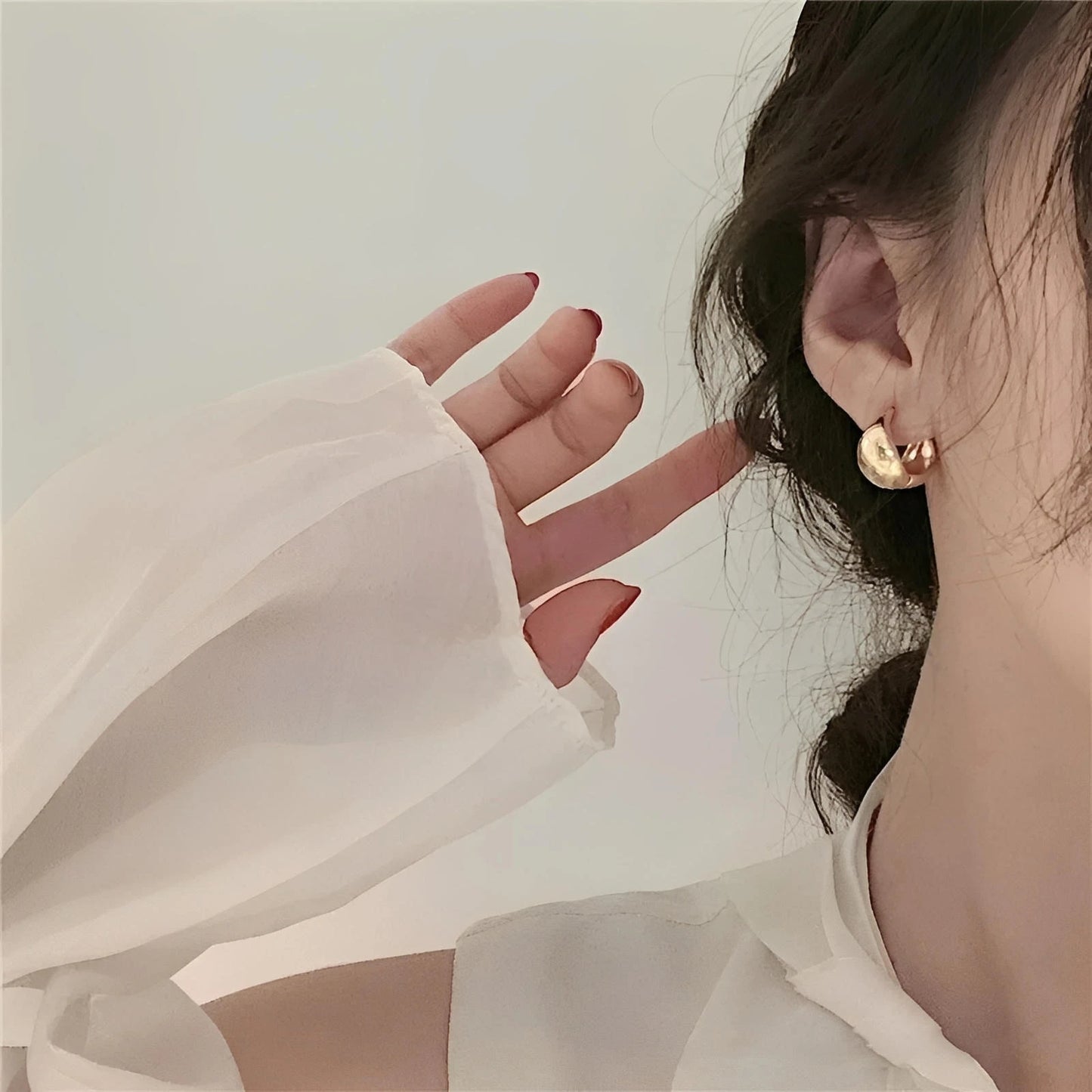 Gold hoop earrings on woman with white blouse and wavy hair