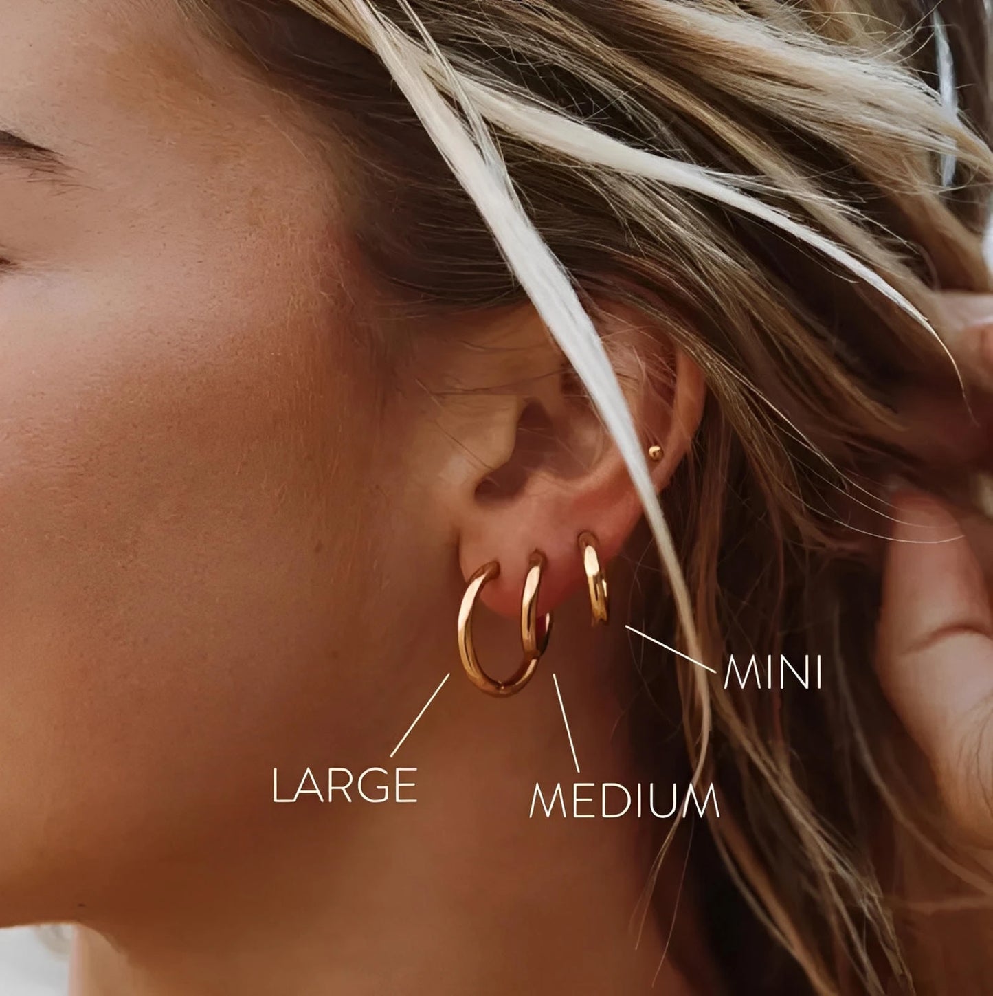 Woman wearing gold hoop earrings in large, medium, and mini sizes on ear
