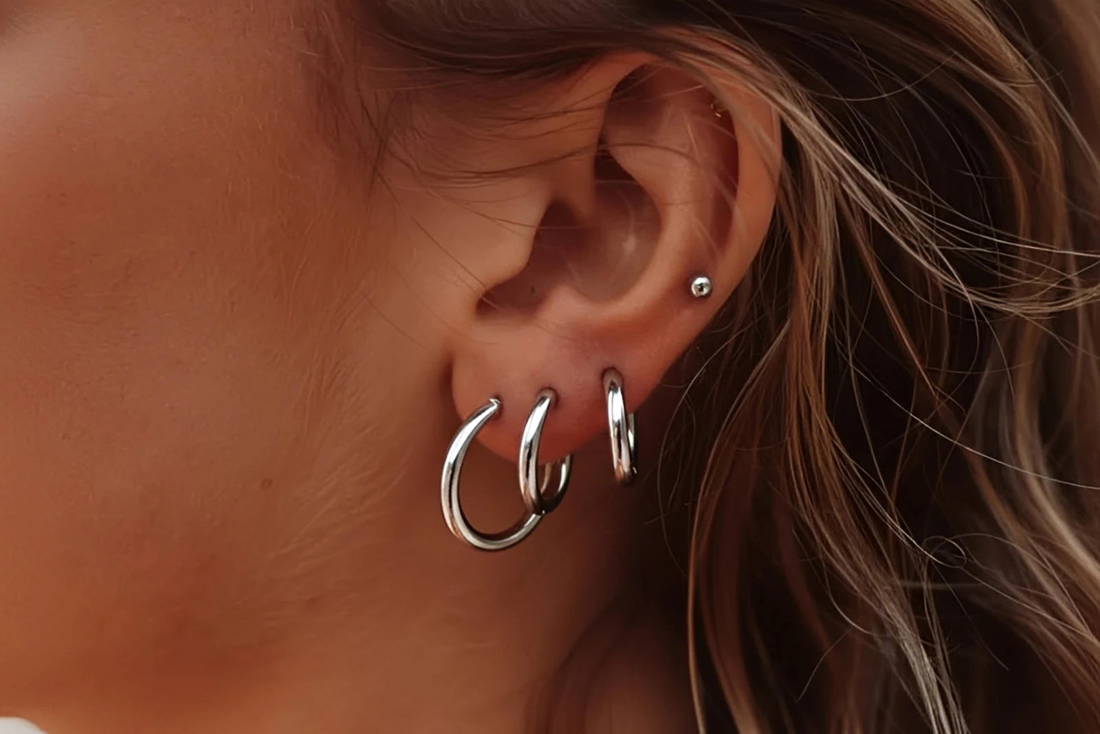 Woman wearing multiple silver hoop earrings and a stud in ear