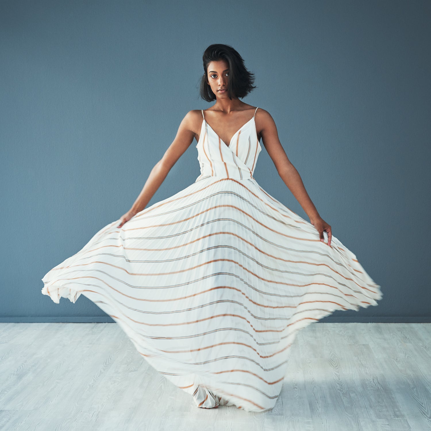 Young woman in a flowing striped maxi dress, posing indoors on a light wood floor