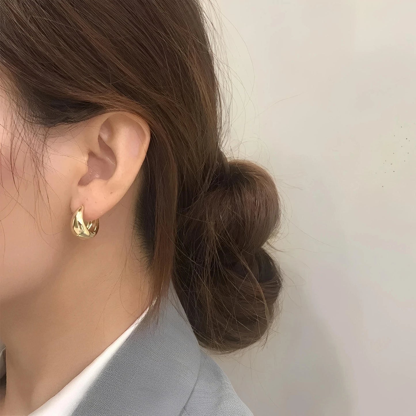 Gold twisted hoop earring on woman with low bun hairstyle, wearing a gray blazer